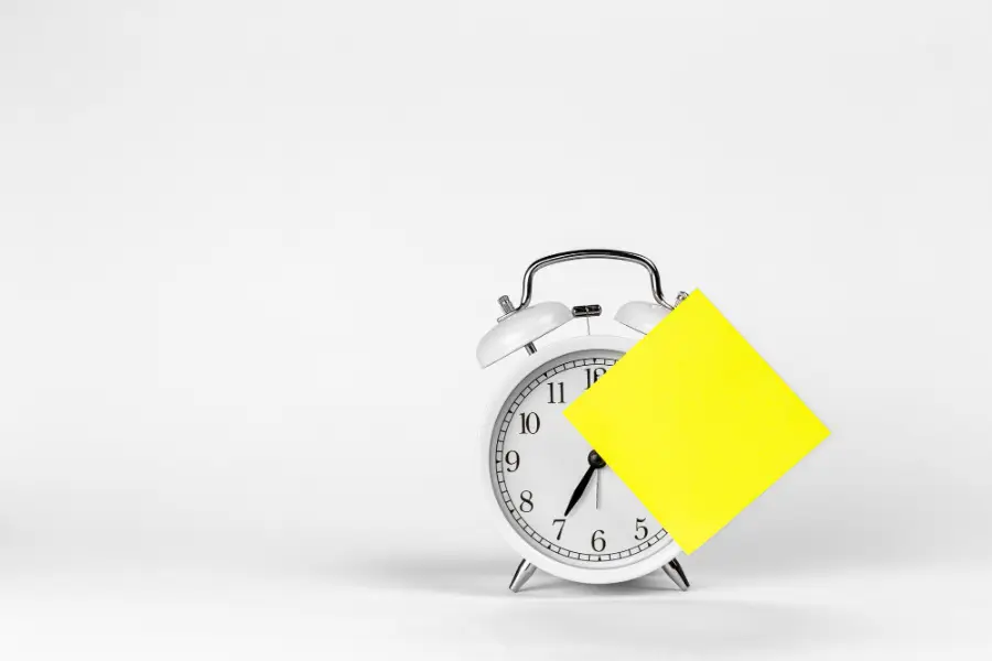 White alarm clock and blank paper reminder on a white background isolated